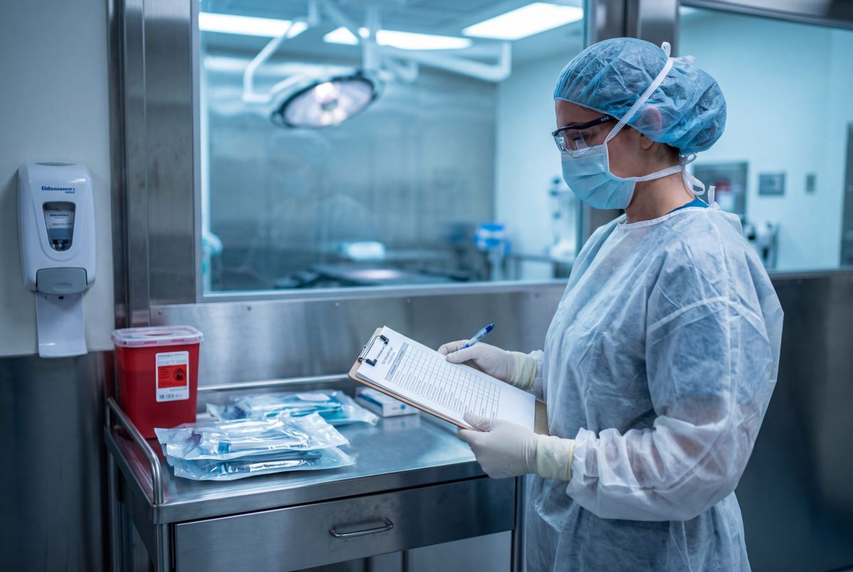 Pielęgniarka epidemiologiczna w jednorazowym fartuchu, maseczce i czepku kontroluje listę sterylnych narzędzi na bloku operacyjnym w szpitalu.
