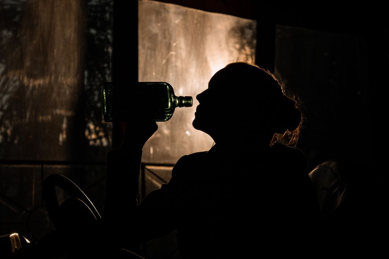 Sylwetka kobiety pijącej alkohol z butelki – problem uzależnienia od alkoholu i potrzeba leczenia nałogu.